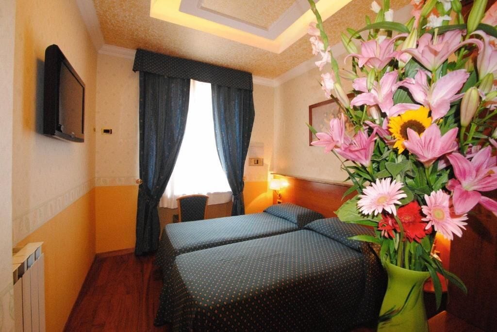 Een hotelkamer met twee bedden, een televisie, een raam met gordijnen, een bureau en een bloevas.