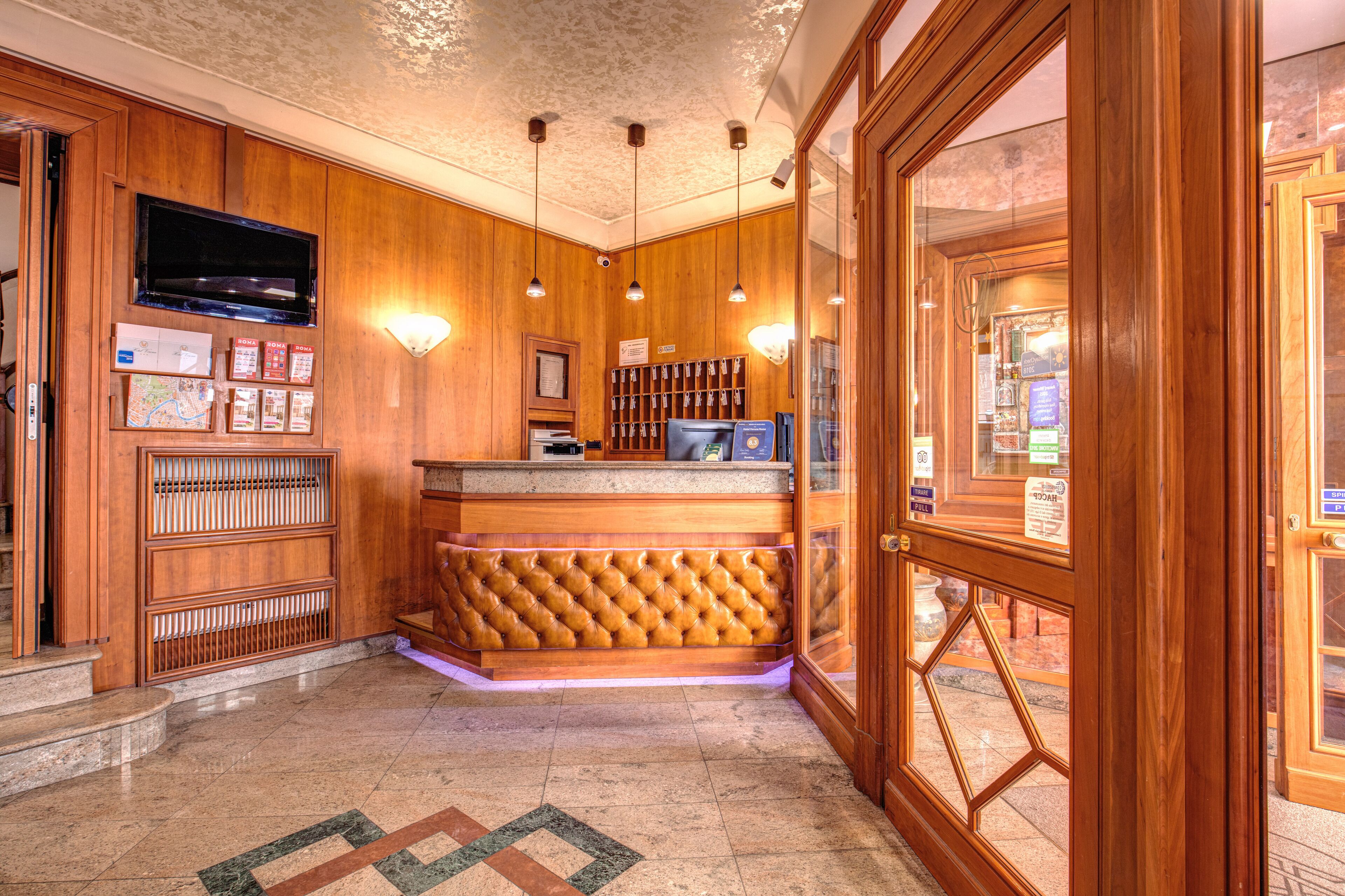 A lobby with a wooden reception desk, a mounted television, and a patterned floor.