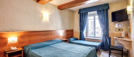 Habitación de hotel con dos camas, un escritorio, una silla, un televisor y una ventana con cortinas.