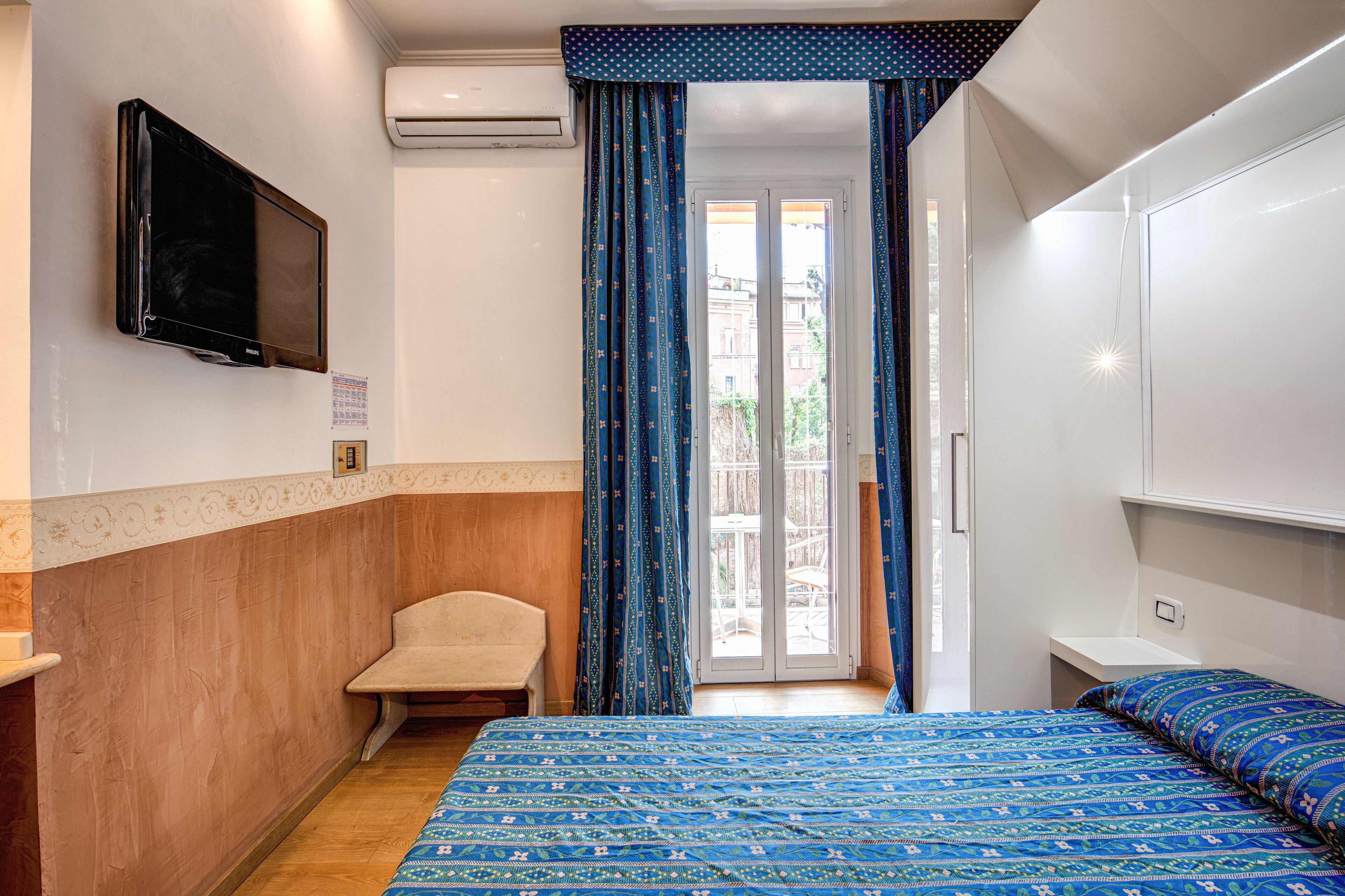 Une chambre avec un lit, une chaise, un téléviseur et une porte-fenêtre coulissante donnant sur un espace extérieur.
