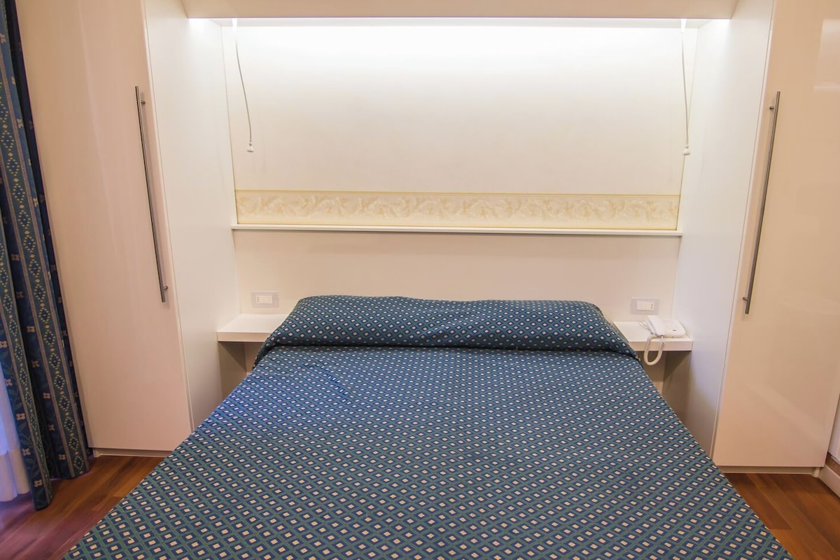A small, compact room with a bed, a bedside table, and a telephone.