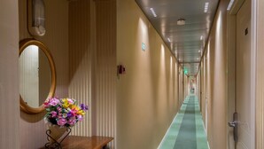 A hotel hallway with a green carpet, wooden benches, a mirror, and a floral arrangement. - Hotel Dorica (Rome)