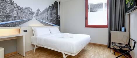 Una habitación de hotel con cama, escritorio, silla y un ventanal grande.