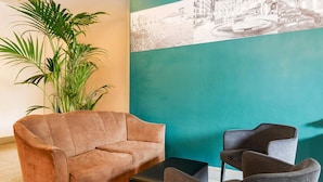 A lobby with a brown sofa, two grey armchairs, a black ottoman, and a large green wall with a historical photo. - B&B Hotel Verona (Verona)
