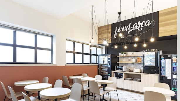 A modern café with round tables and chairs, a kitchen area, and a sign reading "food area". - B&B Hotel Verona (Verona)