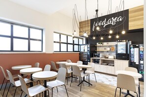 Un café moderno con mesas y sillas redondas, una zona de cocina y un letrero que dice 'food area'.