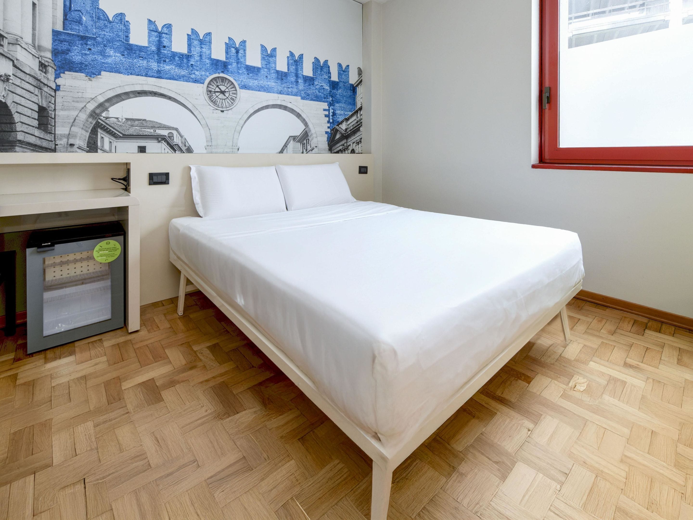 Een slaapkamer met een bed, een klein bureau met stoel, een raam en een muurschildering.