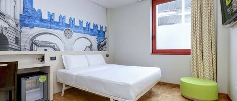 A room with a bed, a small desk, a green ottoman, a window with curtains, and a wall mural.