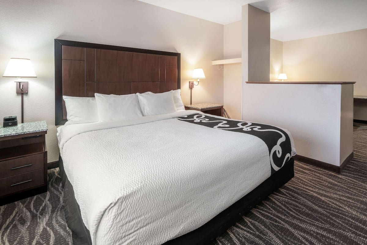 Una habitación de hotel con una cama grande, dos mesitas de noche, un escritorio y dos lámparas de pared.