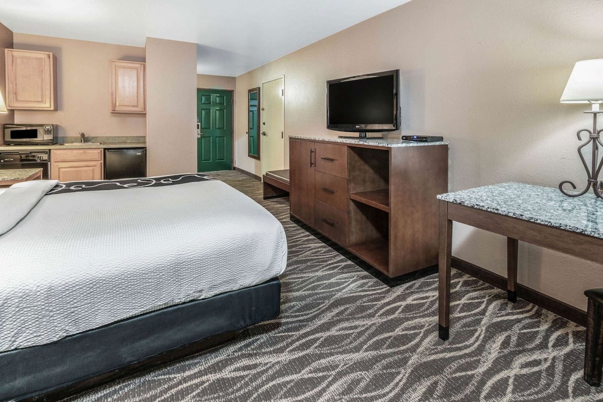 Una habitación de hotel con cama, escritorio, televisor, microondas y kitchenette.