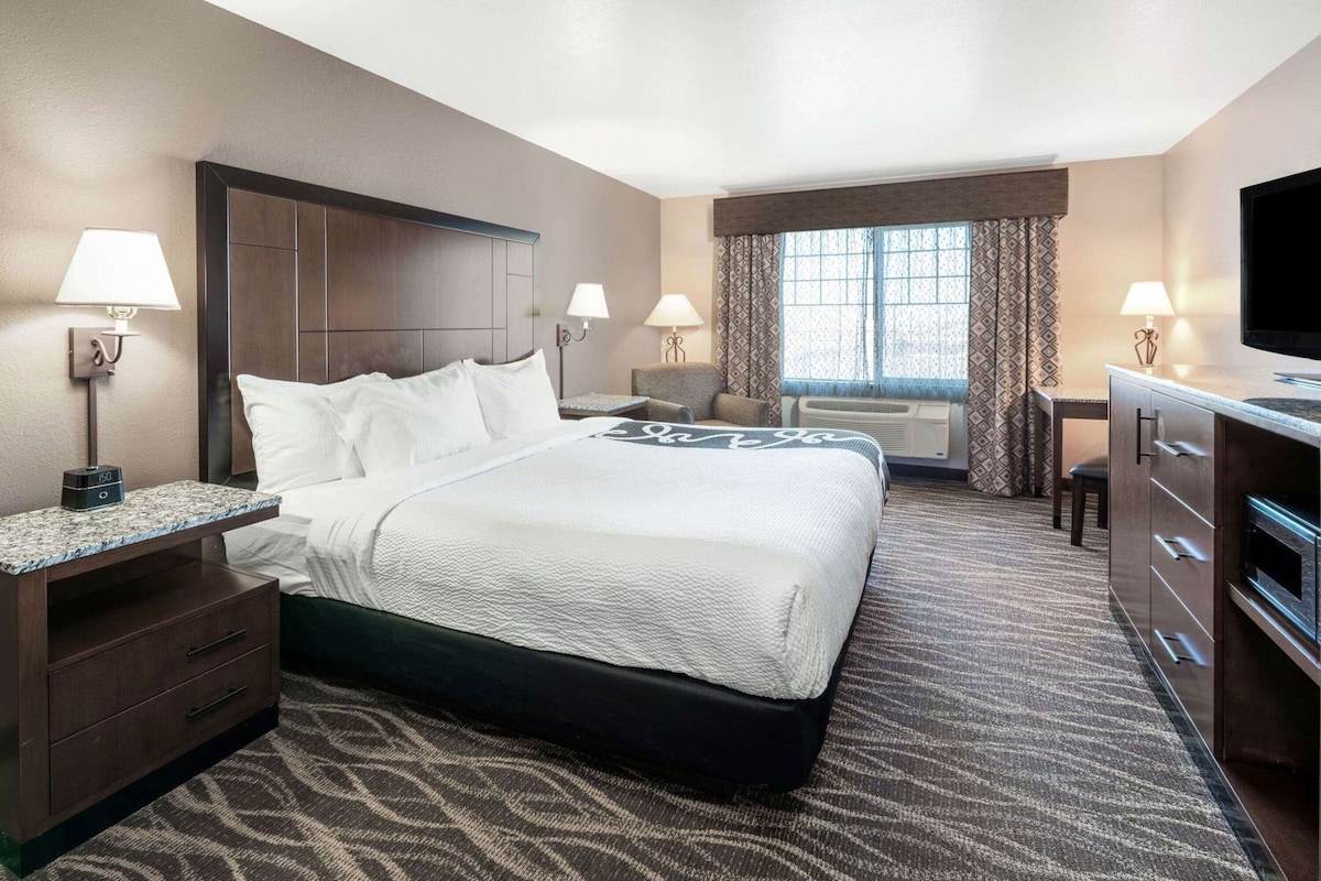 Une chambre d’hôtel avec un grand lit, des tables de chevet, un bureau, une télévision et une fenêtre avec des rideaux.