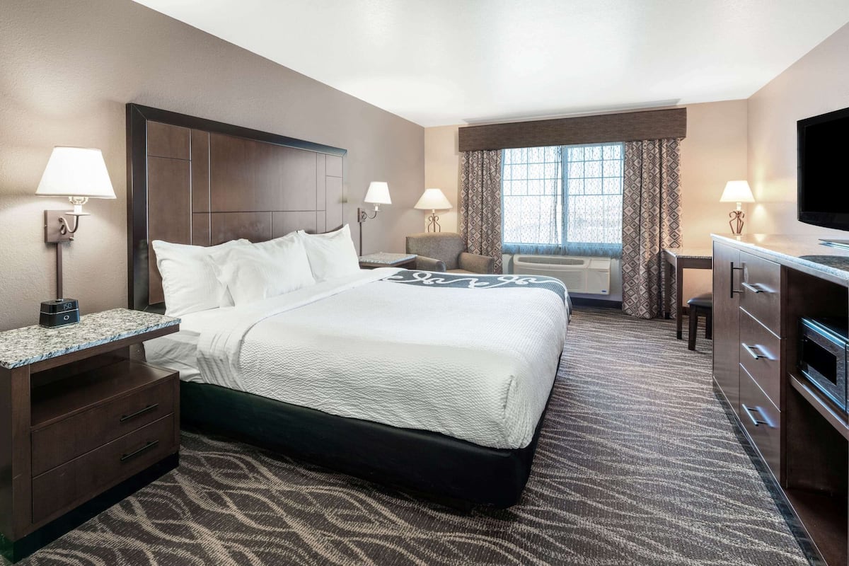 Habitación de hotel con una cama grande, un escritorio, un televisor y una ventana con cortinas.