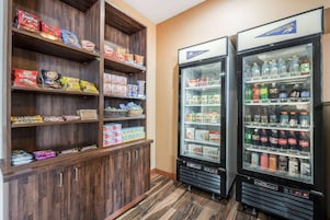 Zona de venta automática con varios estantes llenos de snacks y un refrigerador con diversas bebidas.