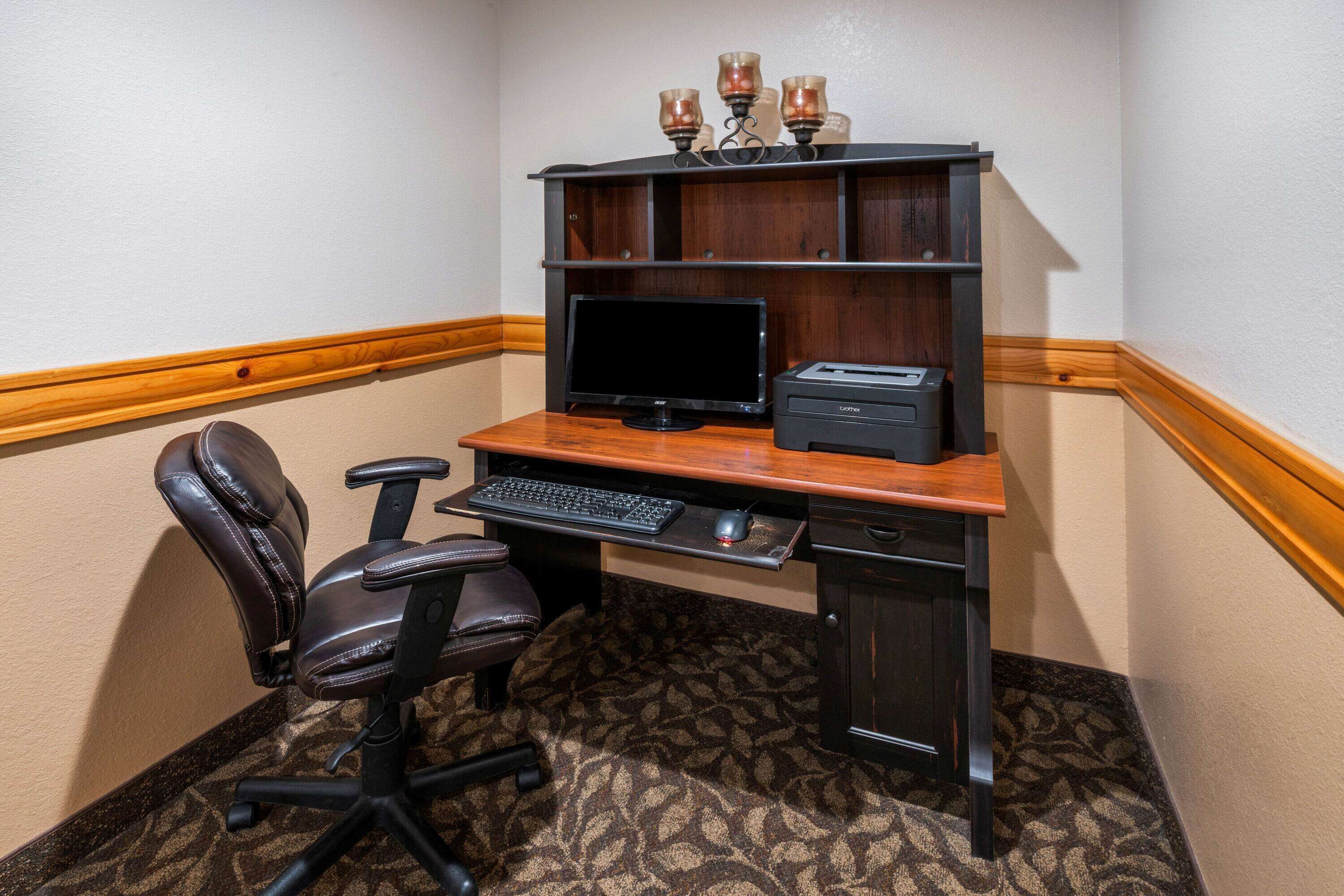 A corner office with a desk, computer, printer, and leather chair.