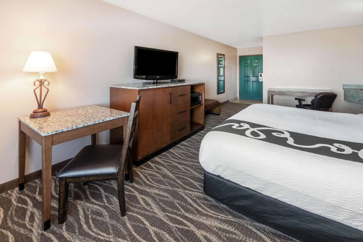 Una habitación de hotel con una cama, un escritorio con lámpara, televisor, cómoda y una silla.