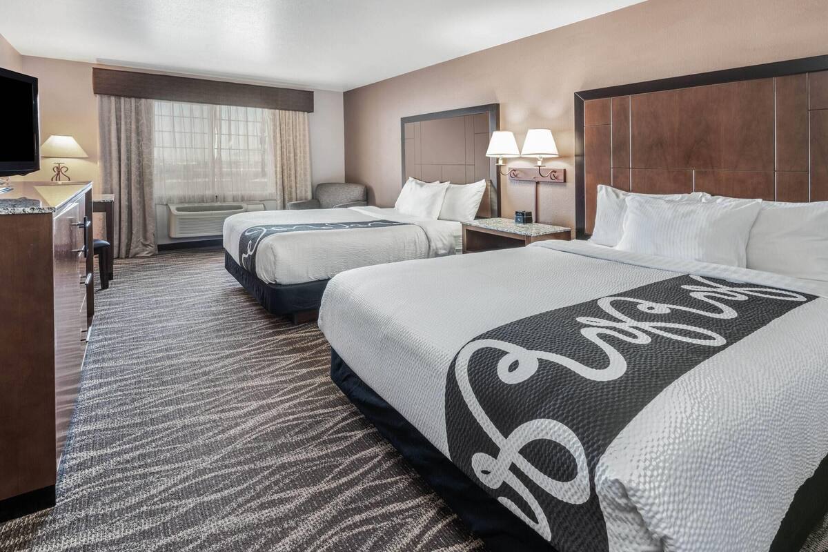 Habitación de hotel con dos camas, un escritorio, un televisor y una ventana con cortinas.