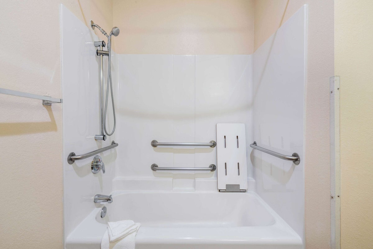Un baño con bañera, barras de apoyo, ducha y toallero.