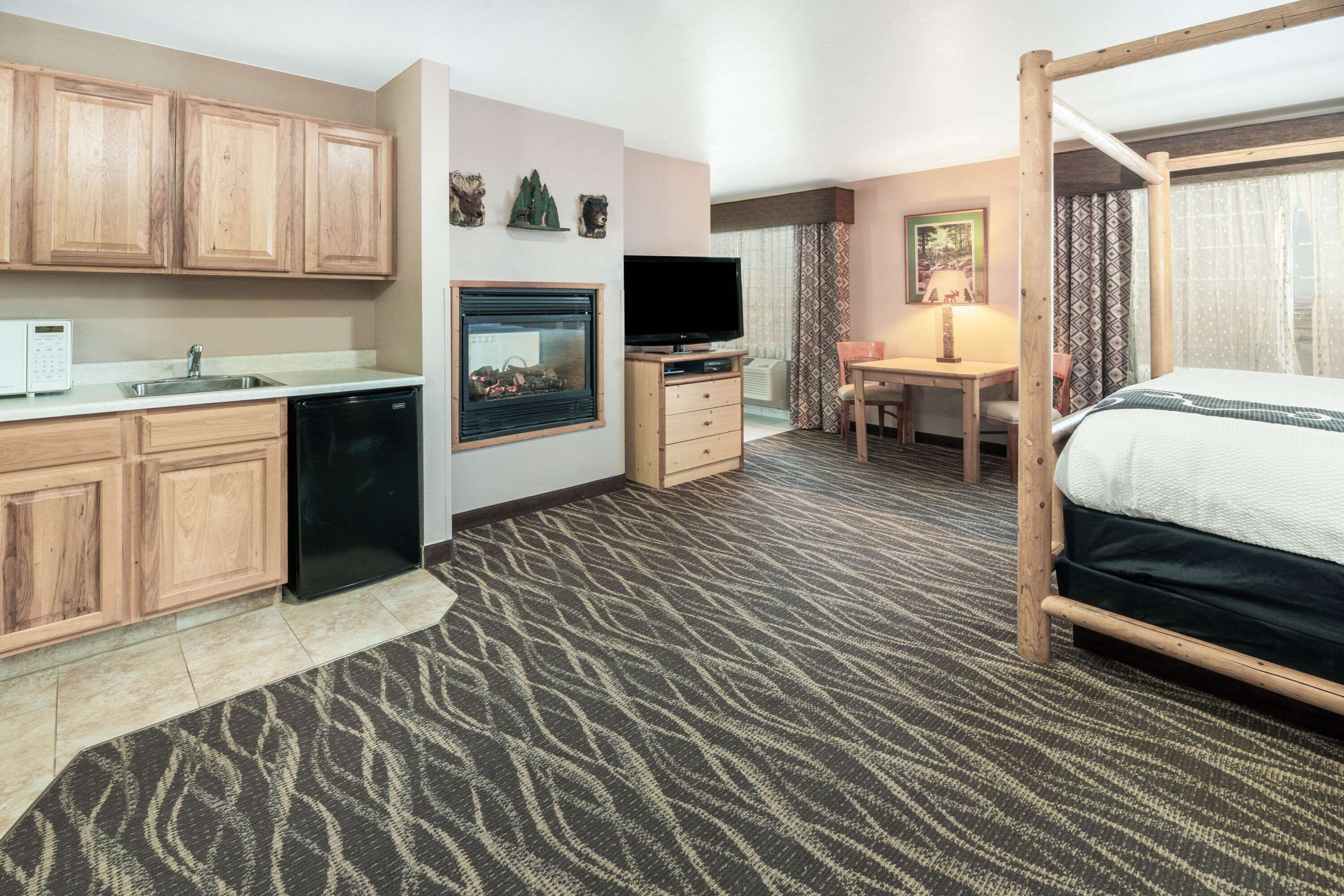 A hotel room with a kitchenette, a bed, a TV, a desk, and a window with curtains.