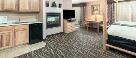 A hotel room with a kitchenette, a bed, a TV, a desk, and a window with curtains.