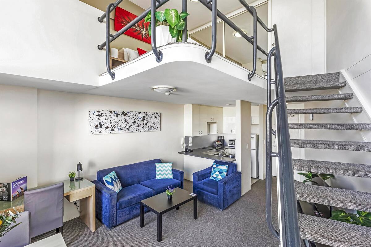 A modern apartment with a living area, kitchen, and a staircase.