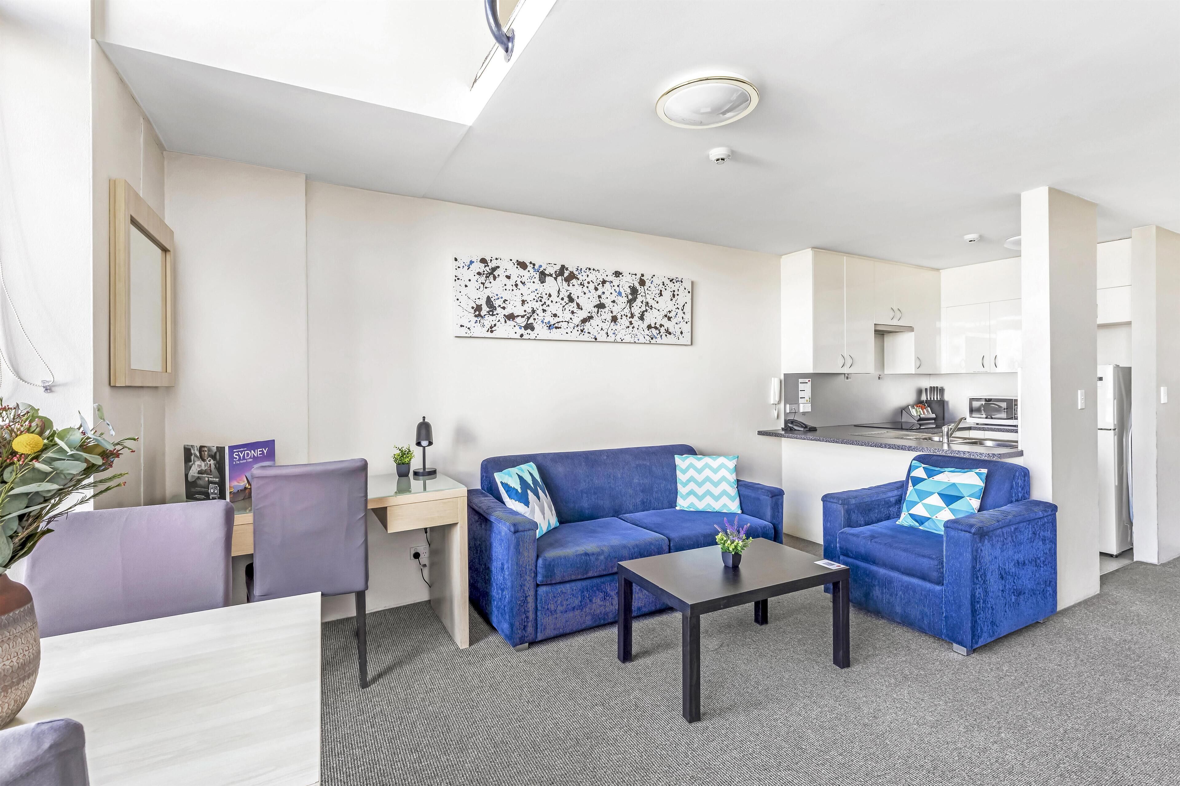 A modern living room with a sofa, two armchairs, a coffee table, and a dining area with a table and chairs.