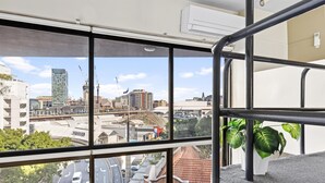 Ein Hotelzimmer in einem Hochhaus mit großen Fenstern und Blick auf die Stadt, einem mit Pflanzen bepflanzten Balkon und einem modernen Interieur.