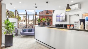 Eine moderne Hotelhalle mit Rezeption, Sitzgelegenheiten und großen Fenstern mit Blick auf die Stadt.