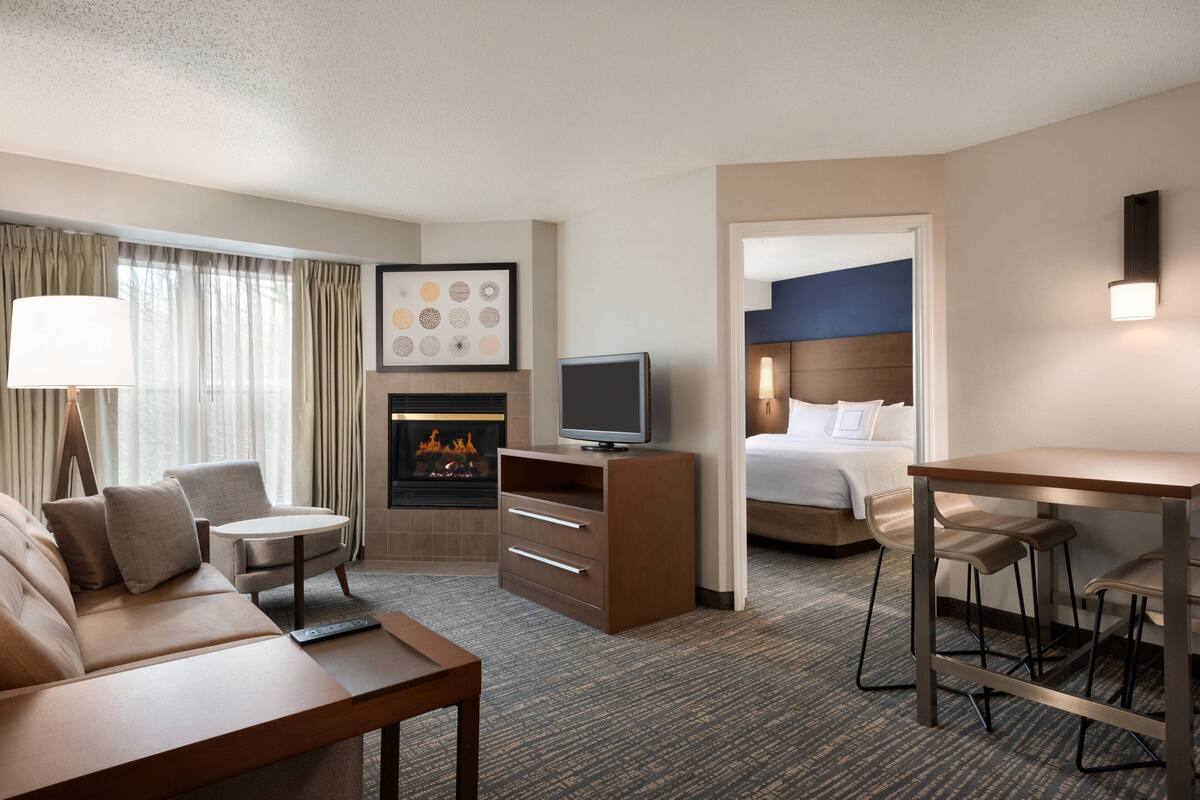 A hotel room with a sofa, TV, fireplace, bed, and a small table with bar stools.
