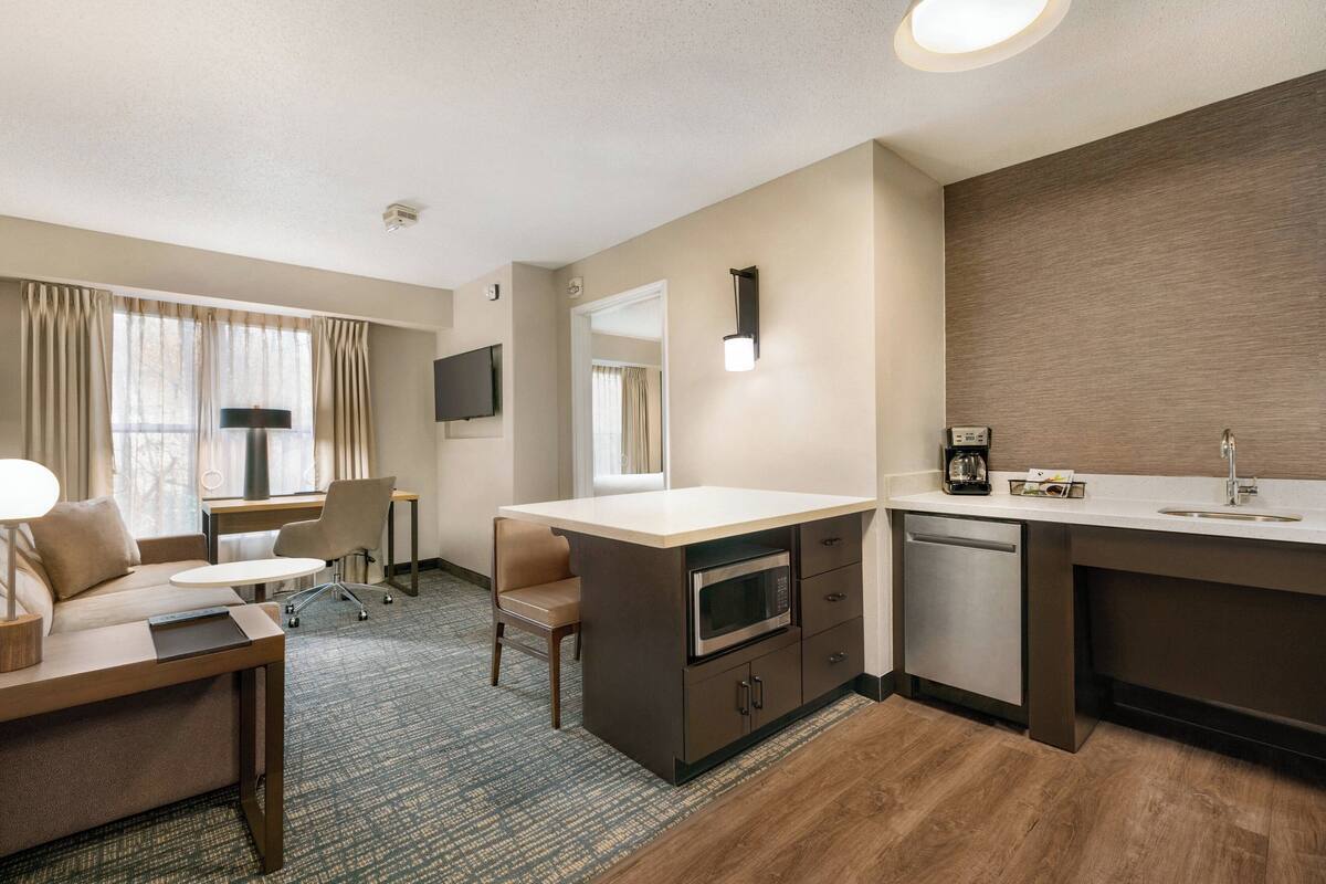 A hotel room with a kitchenette, a sofa, a desk, and a TV.