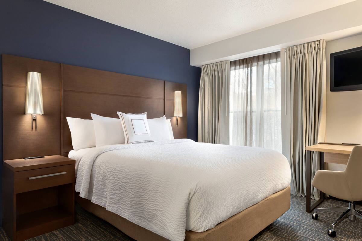A hotel room with a large bed, bedside lamps, a desk, and a TV.