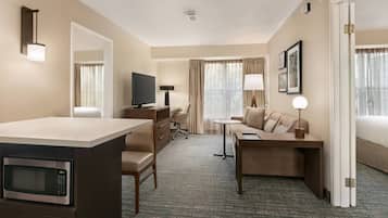 A hotel room with a kitchenette, a TV, a desk, a sofa, and a bed.