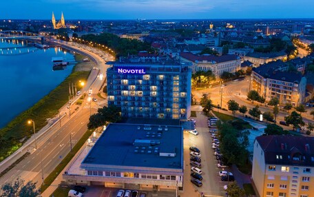 A Novotel hotel with a parking lot, surrounded by city buildings and a river.