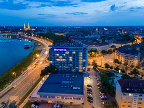 A Novotel hotel with a parking lot, surrounded by city buildings and a river.