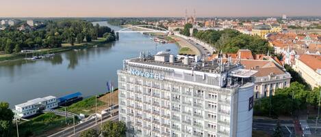 A high-rise hotel with a modern facade, located near a river with a bridge in the background.