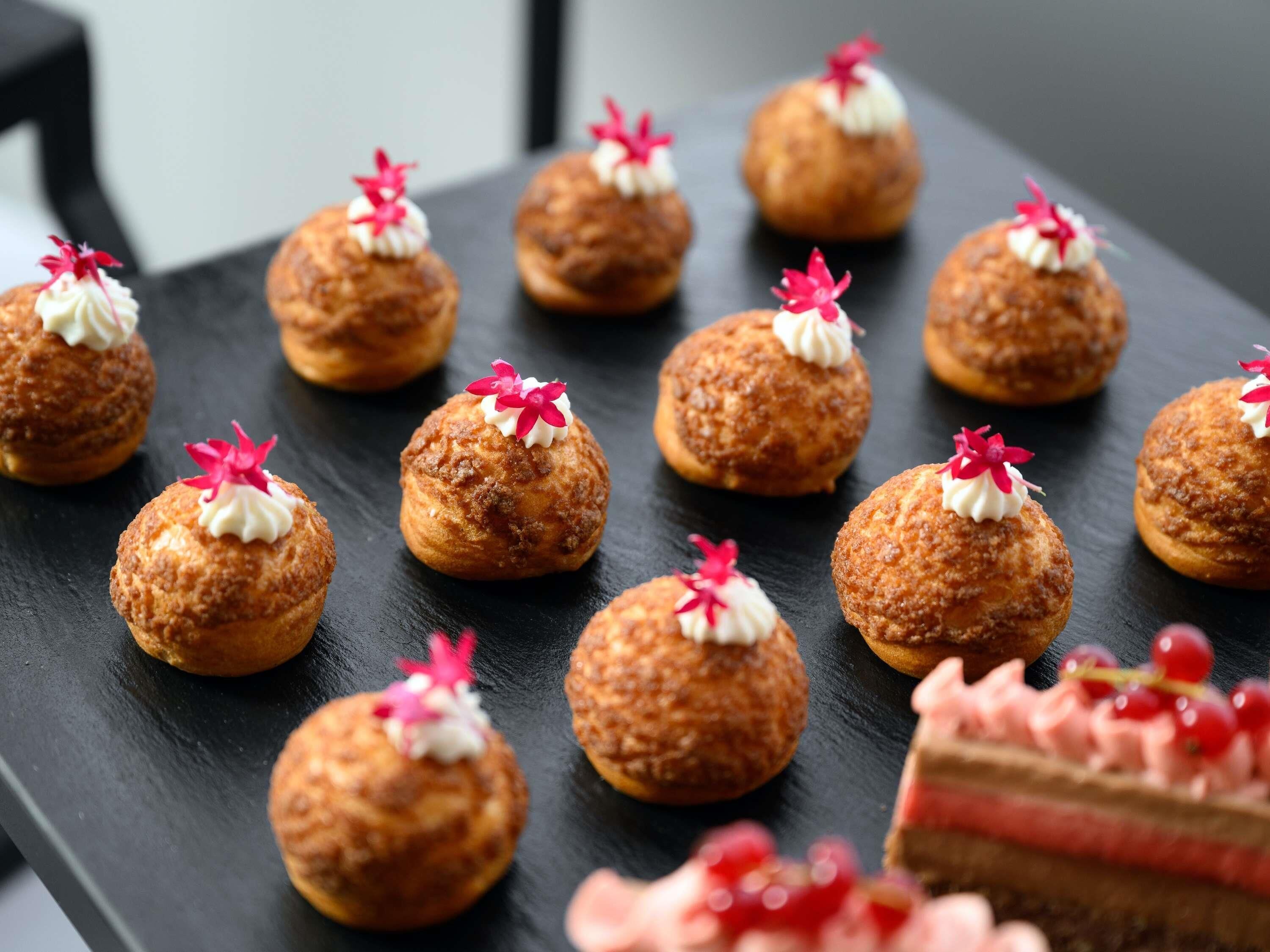 A dessert platter with round pastries topped with cream and a pink flower, on a dark slate surface.