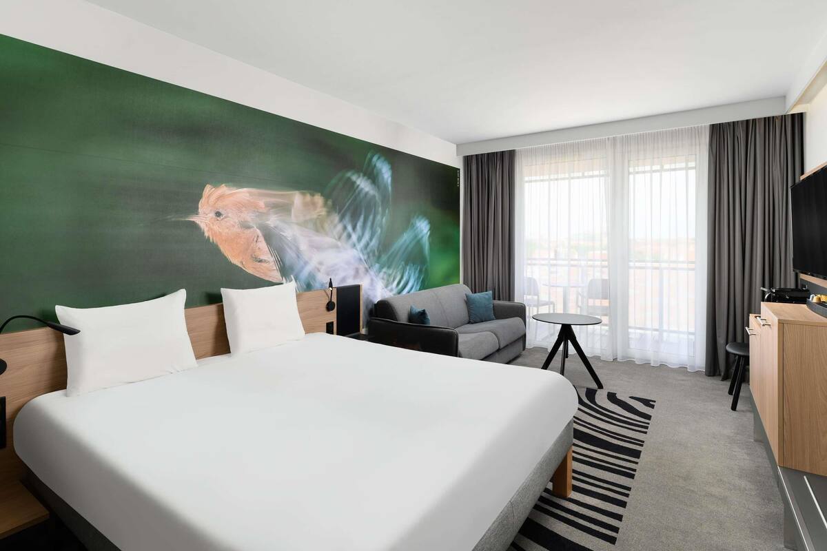 A modern hotel room with a large bed, a sofa, a small table, and a TV.