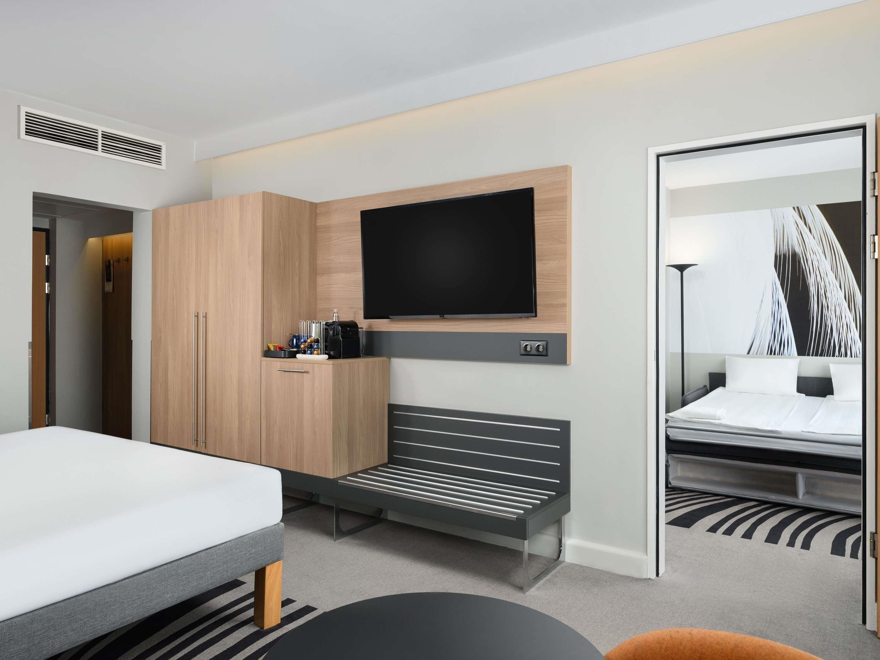 Una habitación de hotel moderna con cama, sofá, televisión montada en la pared y armario.
