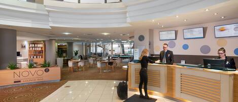 A modern hotel lobby with a reception desk, lounge bar, and seating area.