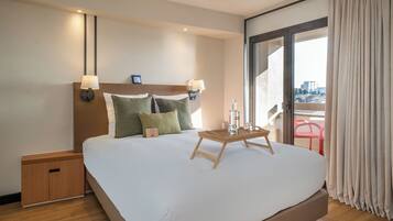 A hotel room with a large bed, a bedside table, a nightstand, a window with curtains, and a view of the city.