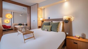 Ein Hotelzimmer mit einem großen Bett, Nachttischen, einem Schreibtisch und einem roten Sessel.
