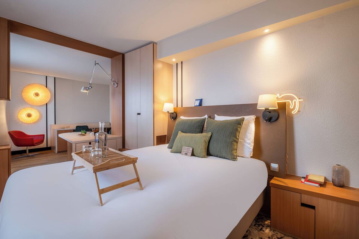 A hotel room with a large bed, bedside tables, a desk, and a red chair.