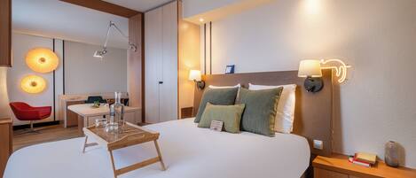 A hotel room with a large bed, bedside tables, a desk, and a red chair.