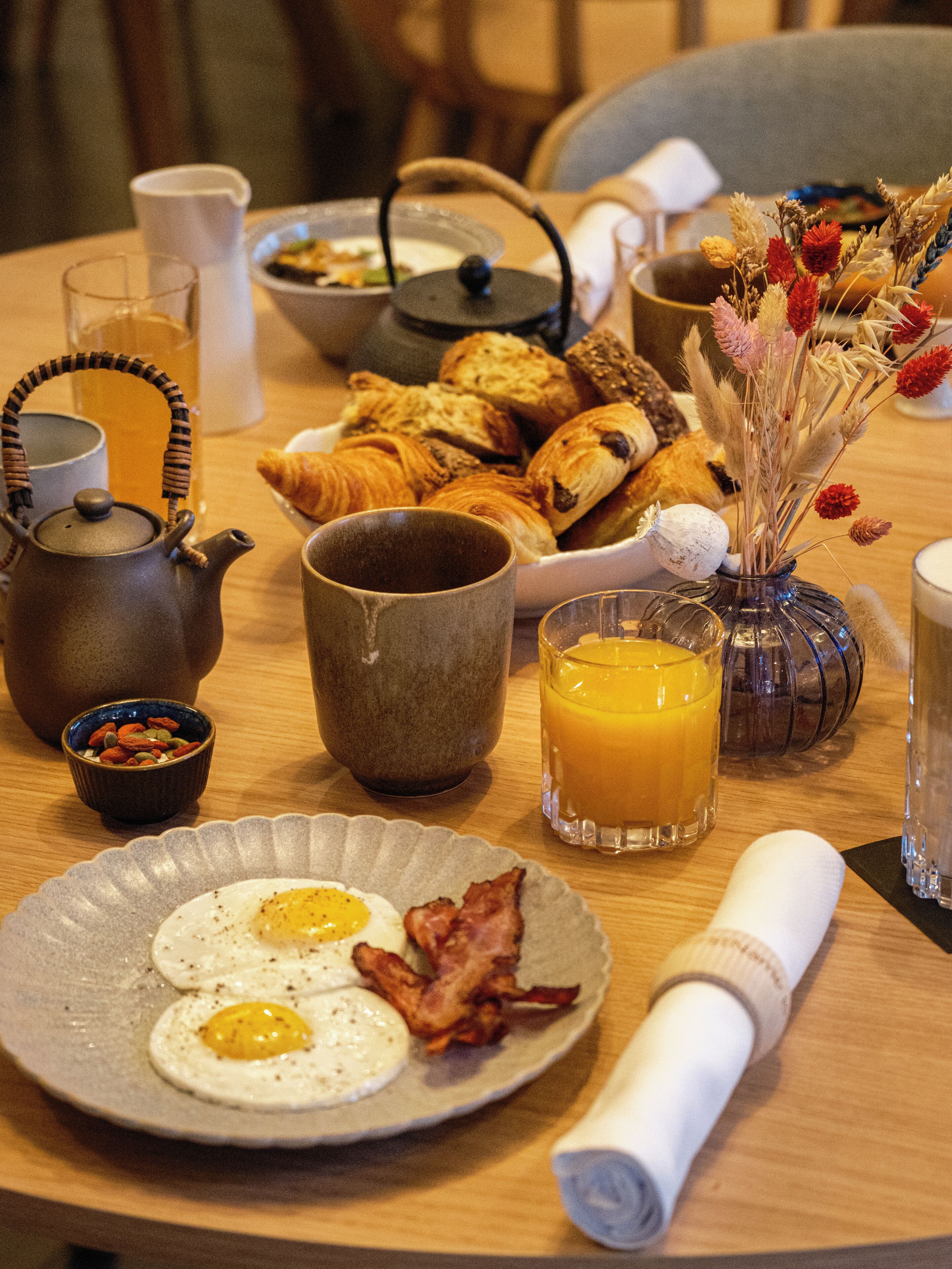A breakfast table with eggs, bacon, pastries, and a teapot.