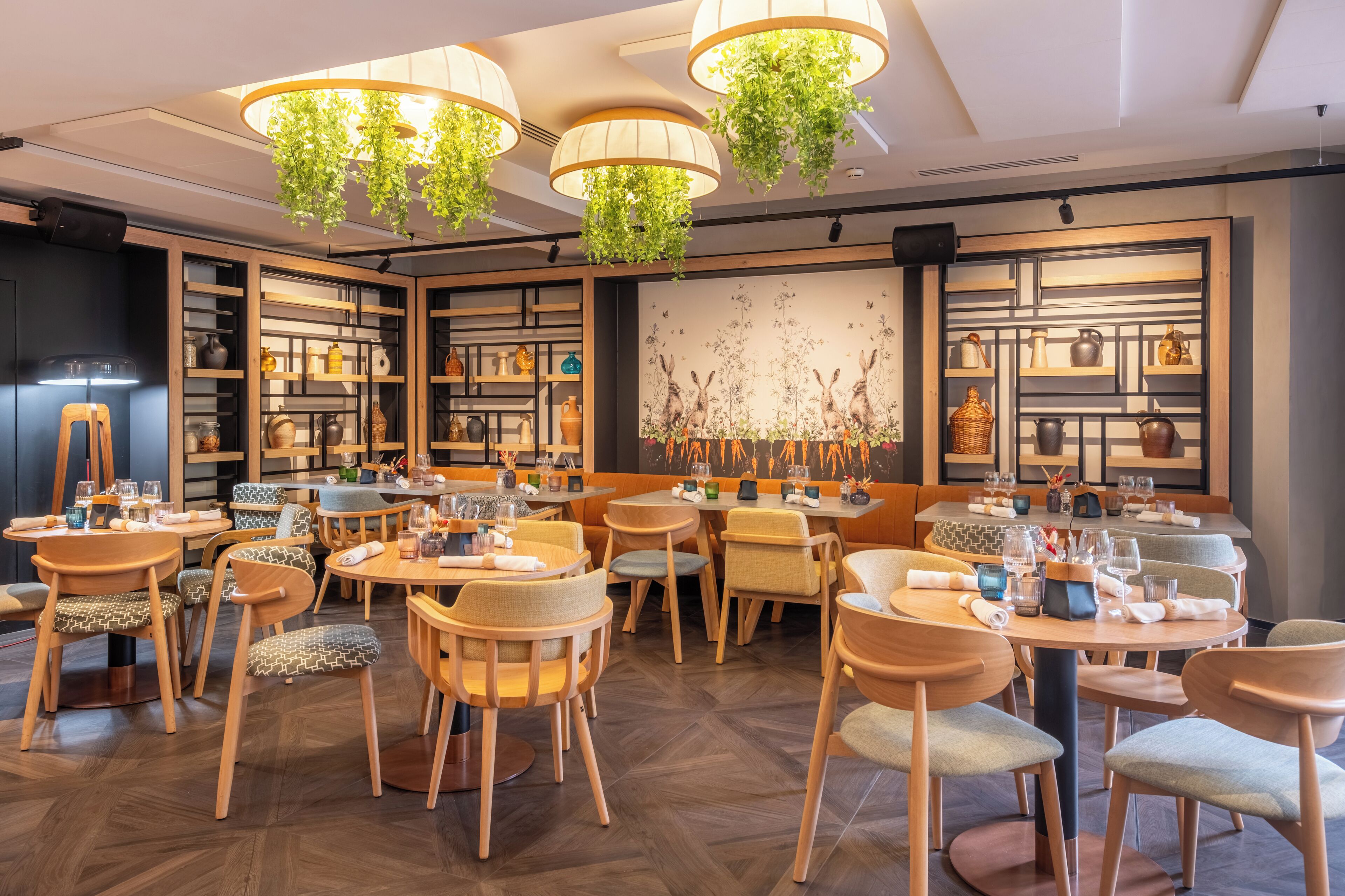 A restaurant with wooden furniture, hanging plants, and shelves with kitchenware.