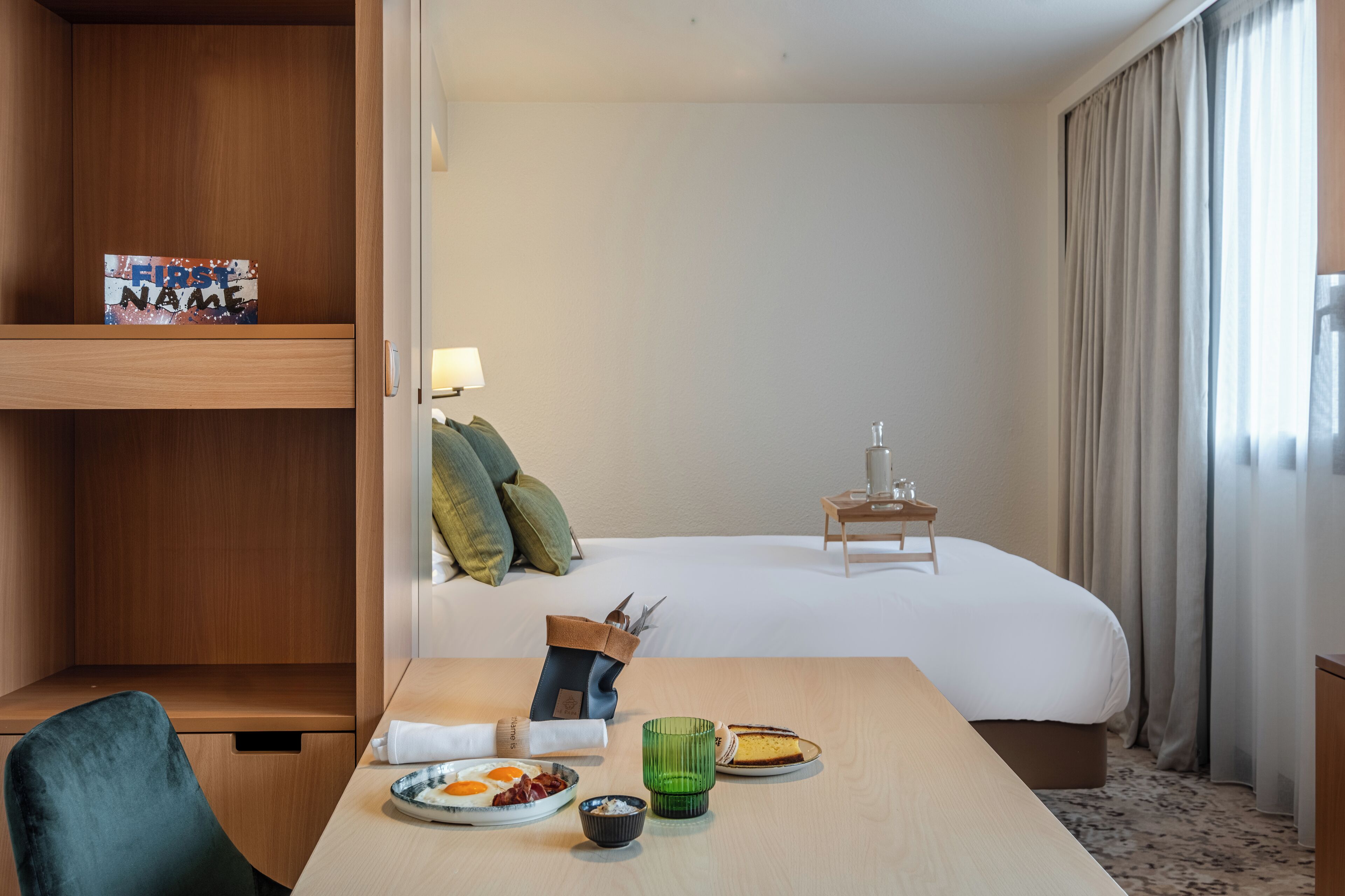 Une chambre d’hôtel avec un lit, un bureau sur lequel se trouve une assiette de nourriture, une lampe et un cadre photo accroché au mur.