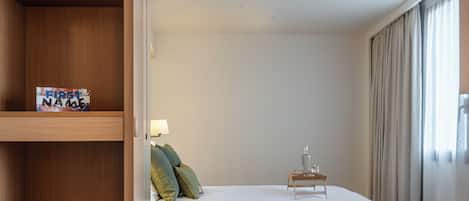 A hotel room with a bed, a desk with a plate of food, a lamp, and a picture frame on the wall.