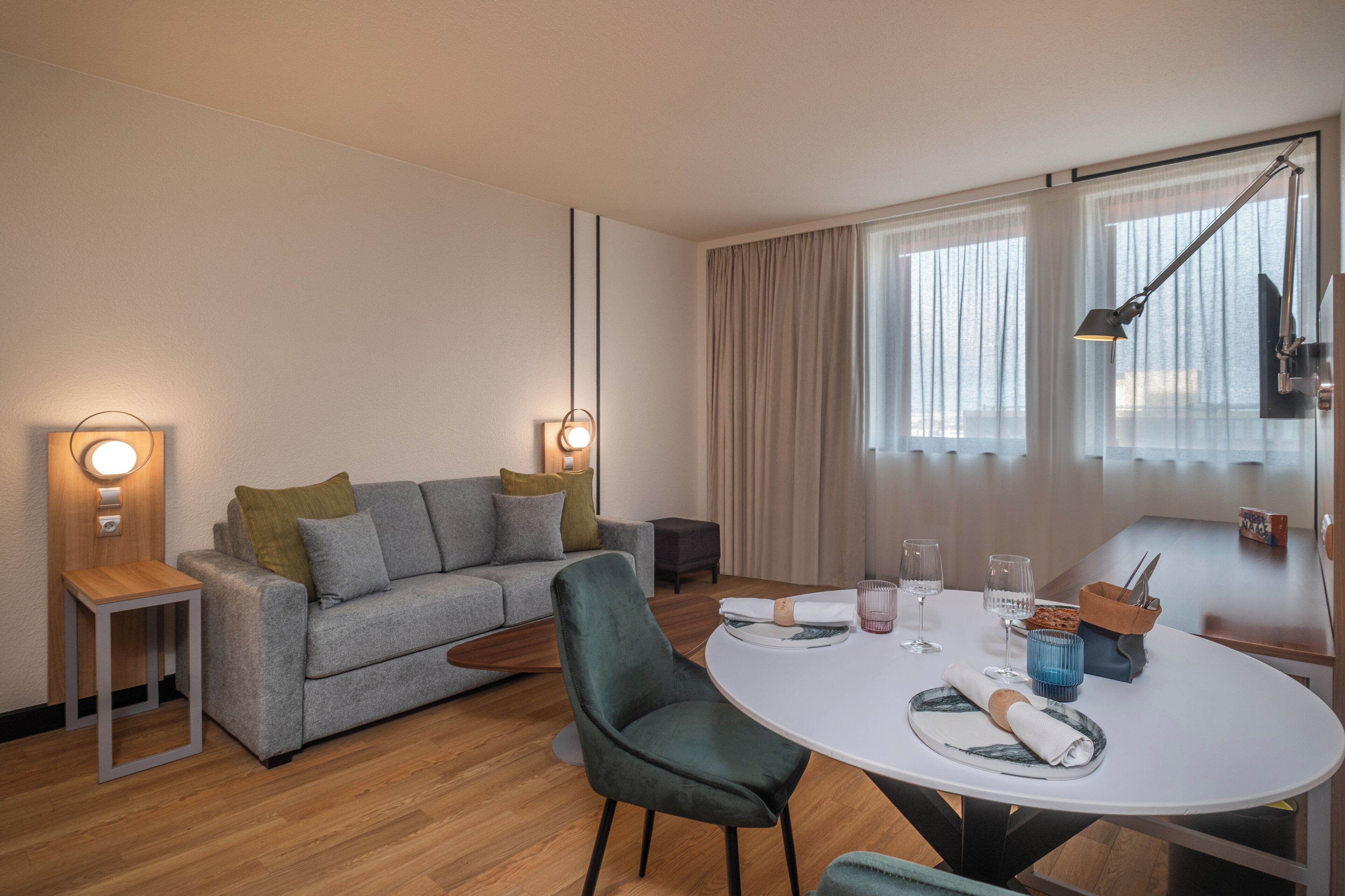A modern living room with a grey sofa, a round dining table, and a green armchair.