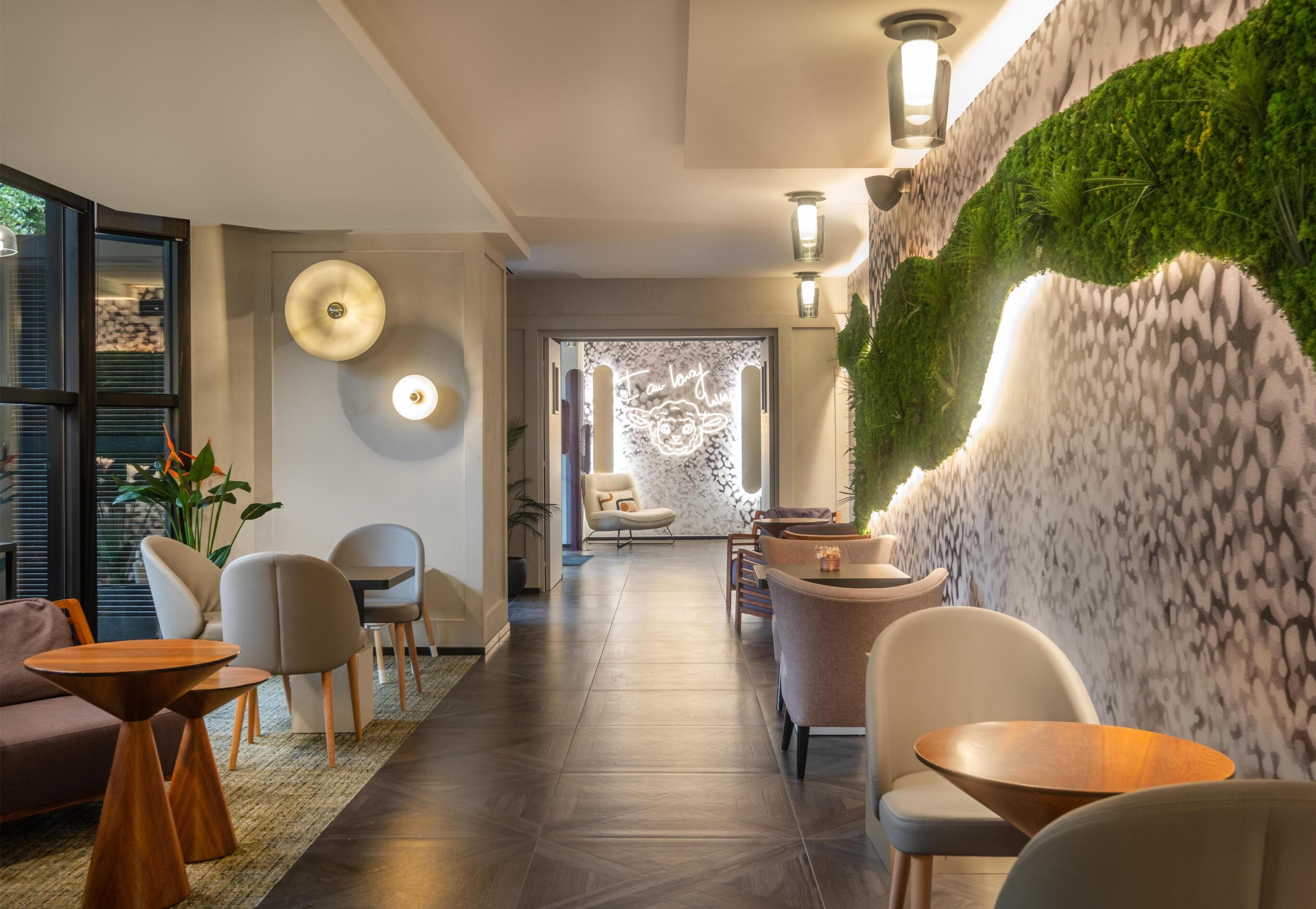 A modern hotel lobby with a reception desk, seating area, and a wall with a green vertical garden.