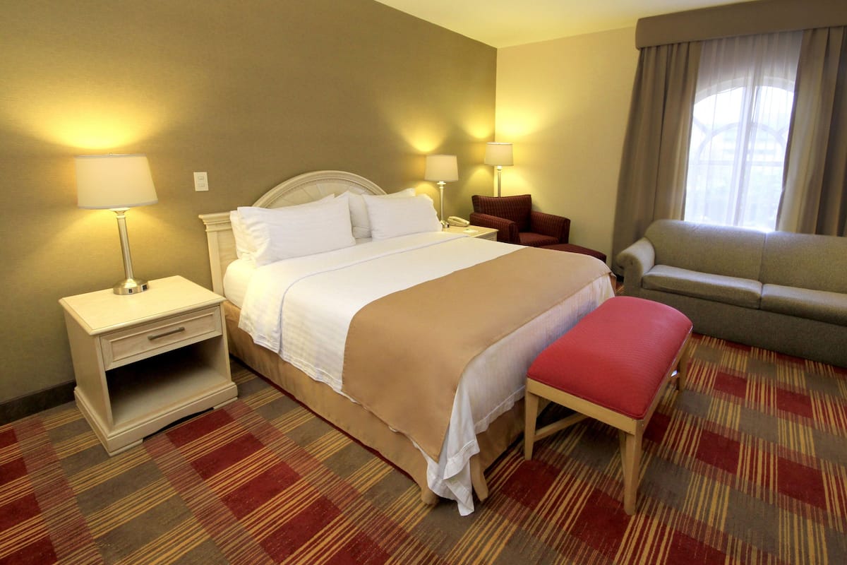 A hotel room with a bed, bedside tables, a chair, a sofa, and a window.