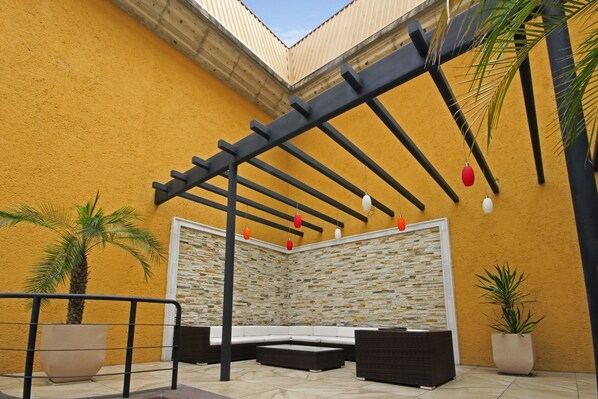 A covered patio area with a stone wall, a white cushioned bench, and a black pergola structure. - Holiday Inn Monclova by IHG (Monclova)